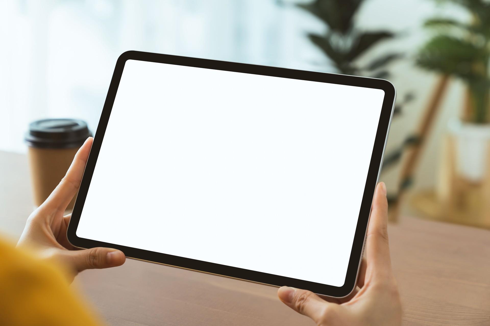 Manos sosteniendo la tableta digital con maqueta de pantalla en blanco en el sofá de la sala de estar.